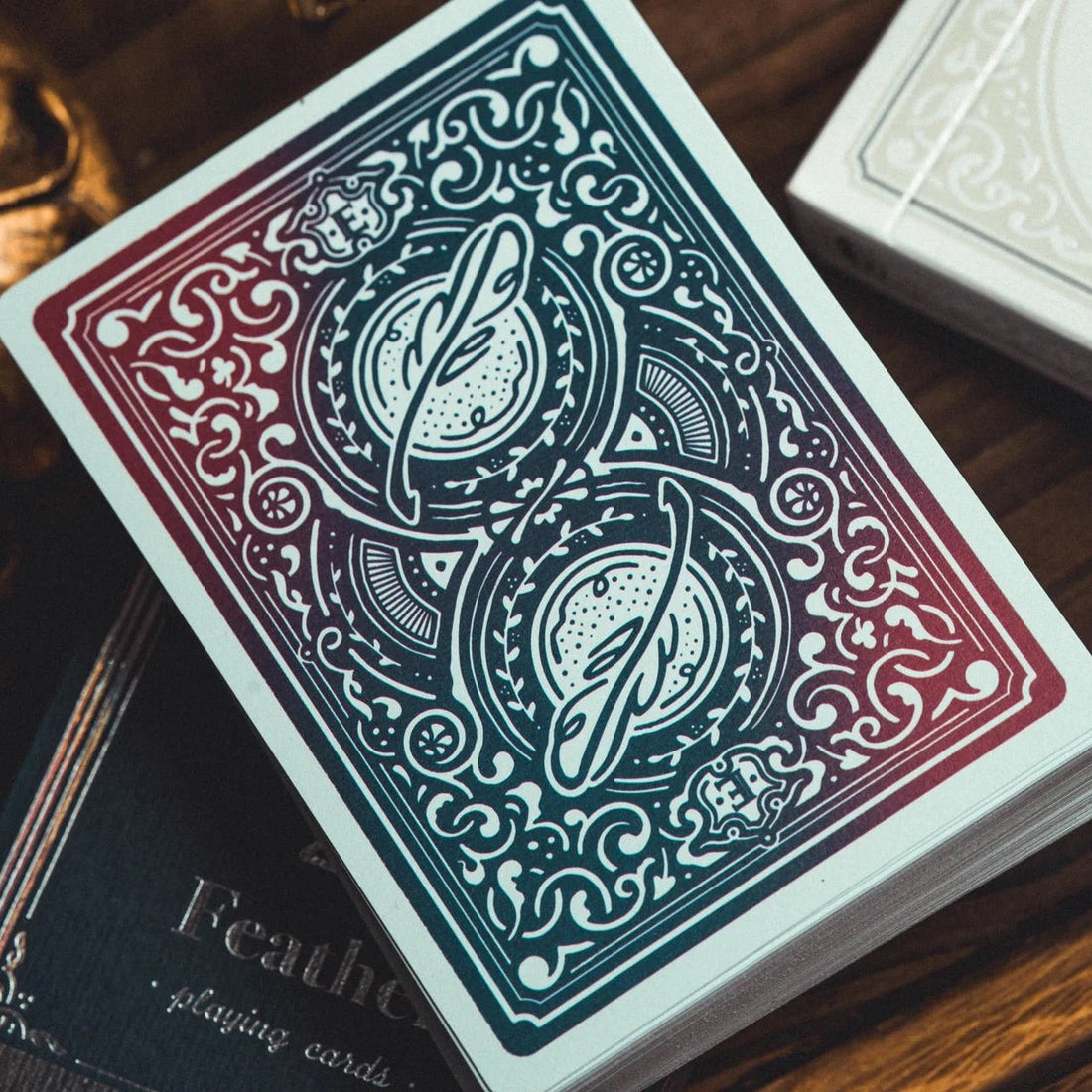 A deck of decorative playing cards with an ornate blue and red patterned back, resting on a wooden surface next to a gold-toned decorative object and another card deck box.