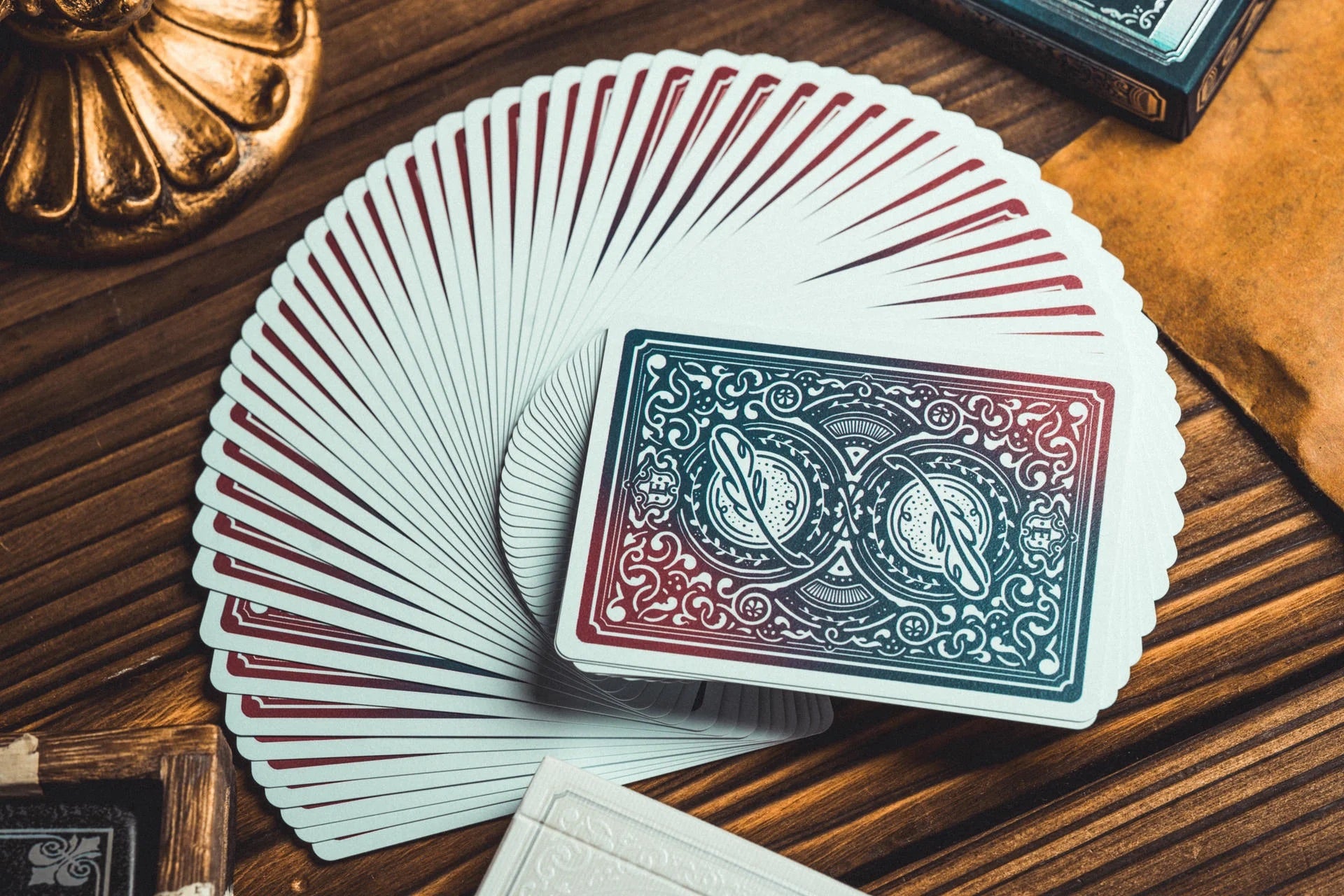 A fan of playing cards spread on a wooden table, with one card face-up in the center showing an ornate blue and red back design.