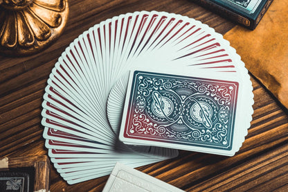 A fan of playing cards spread on a wooden table, with one card face-up in the center showing an ornate blue and red back design.