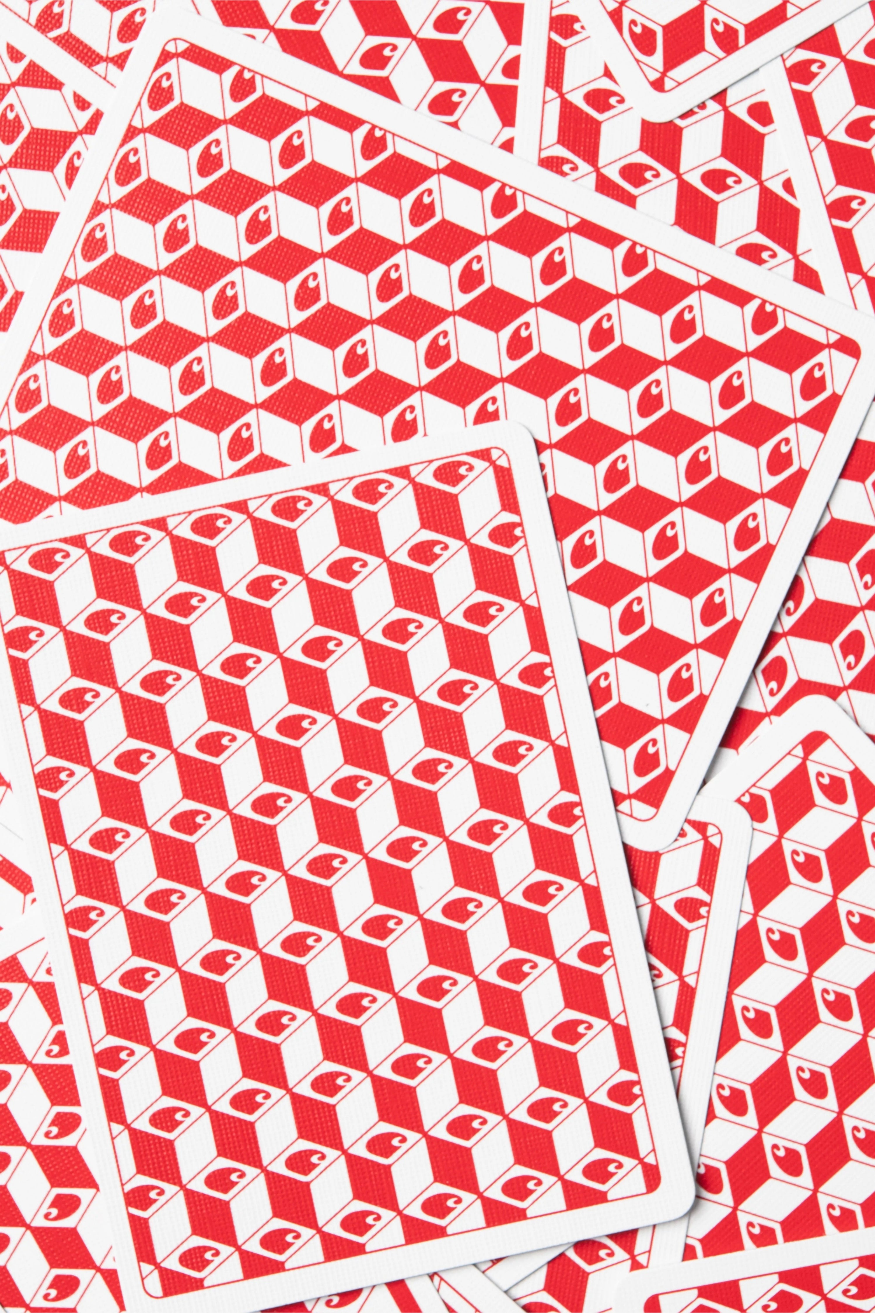 A close-up of several overlapping playing cards showing a repeating red and white geometric cube pattern on the backs.
